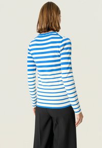 Blå och vit randig långärmad tröja, slim-fit design, rund halsringning, mjuk stickad textur, kombineras med svarta byxor.
