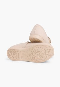 Pantofi din material bej cu fâșie cu arici, design cu vârf rotund și talpă din cauciuc cu modele florale și inimi. Fabricat în Spania.