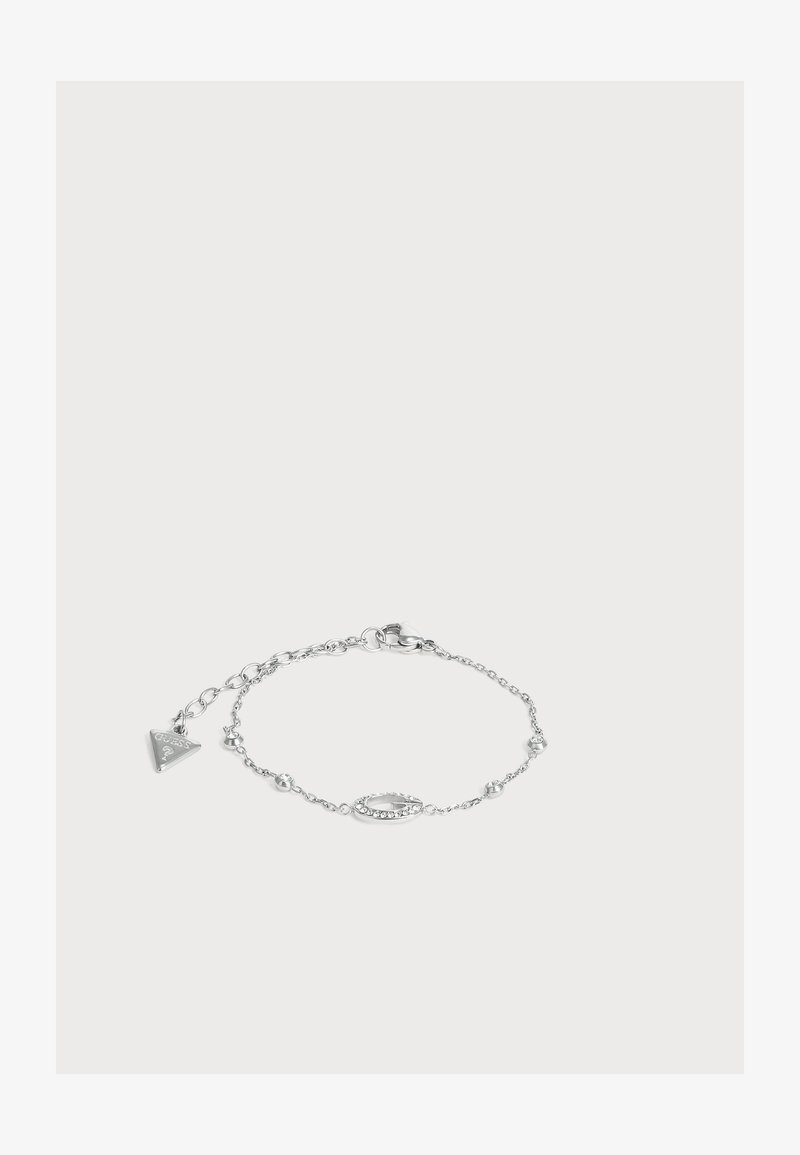 Bracelet délicat en chaîne argentée avec de petites perles, un charm ovale orné de cristaux et une étiquette de marque triangulaire près du fermoir.