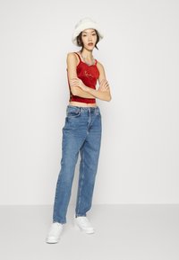 Top corto in velluto rosso con accentuazione in catena, abbinato a jeans a vita alta blu chiaro e sneaker bianche, indossato con un cappello bianco fluffy.