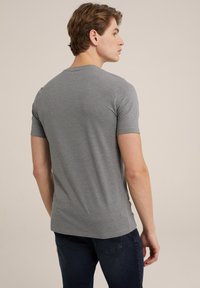 Camiseta gris de manga corta, con cuello redondo y diseño ajustado. Tejido suave y liso con costuras mínimas. Se lleva con jeans de color azul oscuro.