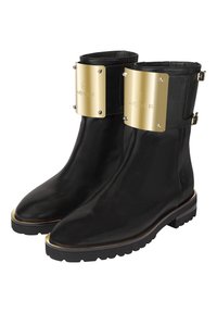 Mustat nahkasaappaat nilkkakorkeudella, joissa on kiiltävä kultainen varustelu, mukaan lukien näkyvä kultalevy varresta ja tekstuuri kumipohja.