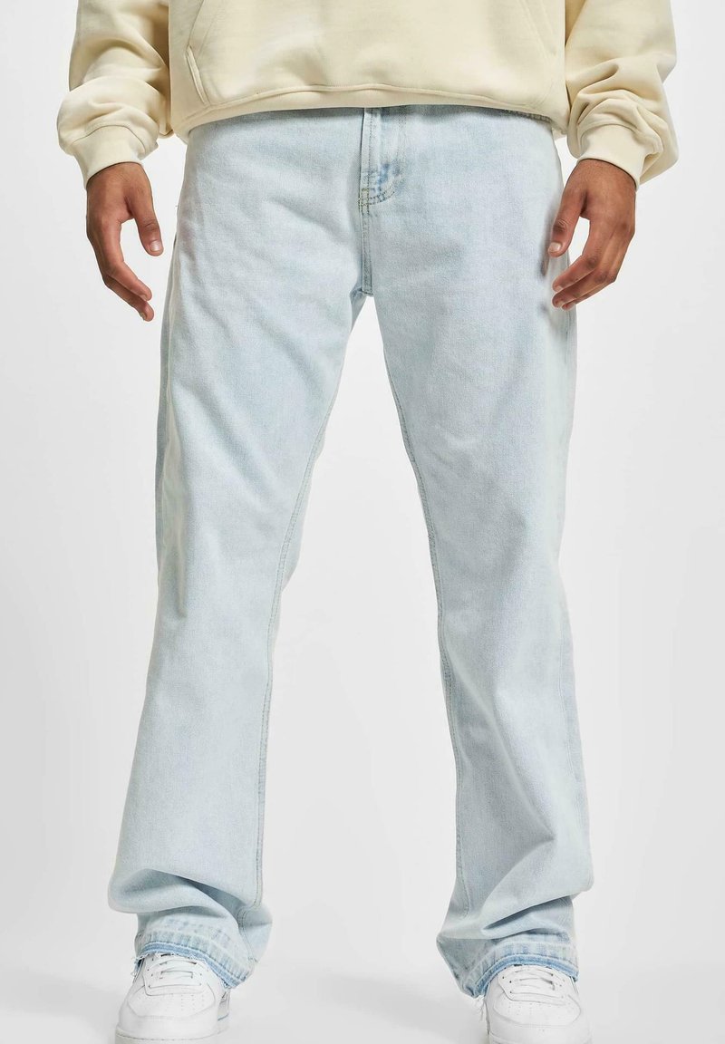 Jeans en denim bleu clair avec une coupe décontractée, des jambes droites et une décoloration subtile. Associés à des baskets blanches pour le contraste.