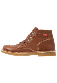 Bottines en cuir marron avec finition texturée, bout rond et couture blanche. Présente des œillets en métal et une semelle en caoutchouc avec un petit talon.