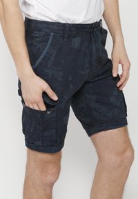 Marineblå cargoshorts i vävt tyg med ett subtilt geometriskt mönster, justerbar midja och flera fickor med tryckknappar.