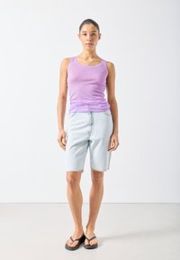 Fioletowy bezrękawnik i jasnoniebieskie dżinsowe szorty z postrzępionym dołem, noszone z czarnymi klapkami. Prosty, swobodny strój.