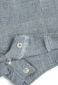 Tissu à carreaux bleu et blanc avec un motif texturé. Présente des boutons-pression argentés et des coutures contrastantes le long des bords.