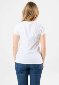 Witte kortemouwen t-shirt van zacht materiaal, met een aansluitend ontwerp. Draagt een spijkerbroek in een blauwe kleur, met weergave van de achterkant en natuurlijk haar dat valt.