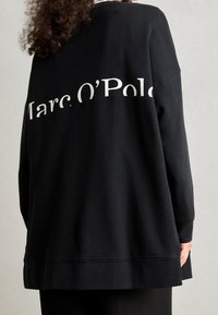 Czarna, oversize bluza z białym nadrukiem logo "Marc O'Polo" na plecach. Wykonana z miękkiego, teksturowanego materiału o luźnym kroju.