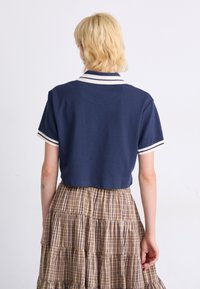 Navy short-sleeve polo shirt with white stripes on collar and sleeves, paired with a tiered plaid skirt in brown tones.