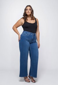 Zwarte tanktop gecombineerd met hoog-wijdse, lichtblauwe, brede jeans. De textuur lijkt glad en de jeans hebben voorzakken en een losse pasvorm.