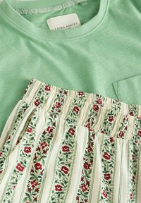 Īsām piedurknēm zaļgani pelēka augšdaļa ar kabatu, kombinēta ar krēmkrāsas elastīgas jostasvietas šortiem ar ziedu rakstu, sarkanām rozēm un zaļiem akcentiem.