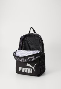 Sac à dos en nylon noir avec un couvercle à motif montagne, présentant un grand logo Puma argenté à l'avant et une poche latérale en mesh.