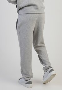 Graue Sweatpants mit einer lockeren Passform, ausgestattet mit einem elastischen Bund und seitlichen Taschen. Kombiniert mit hellgrauen Turnschuhen.