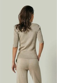 Beige Strickpullover mit kurzen Ärmeln, gerippter Textur und schmaler Passform, kombiniert mit passenden beigen Hosen, die mit einem dezenten Musterakzent versehen sind.