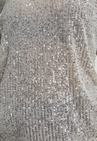 Tissu à sequins argentés avec des rangées verticales denses de petits disques réfléchissants créant une surface scintillante et texturée.