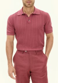 Polo shirt lavorato a maglia di un rosa scuro con un motivo a righe verticali testurizzate, abbinato a pantaloni su misura dello stesso colore, con pince frontale e passanti per cintura.