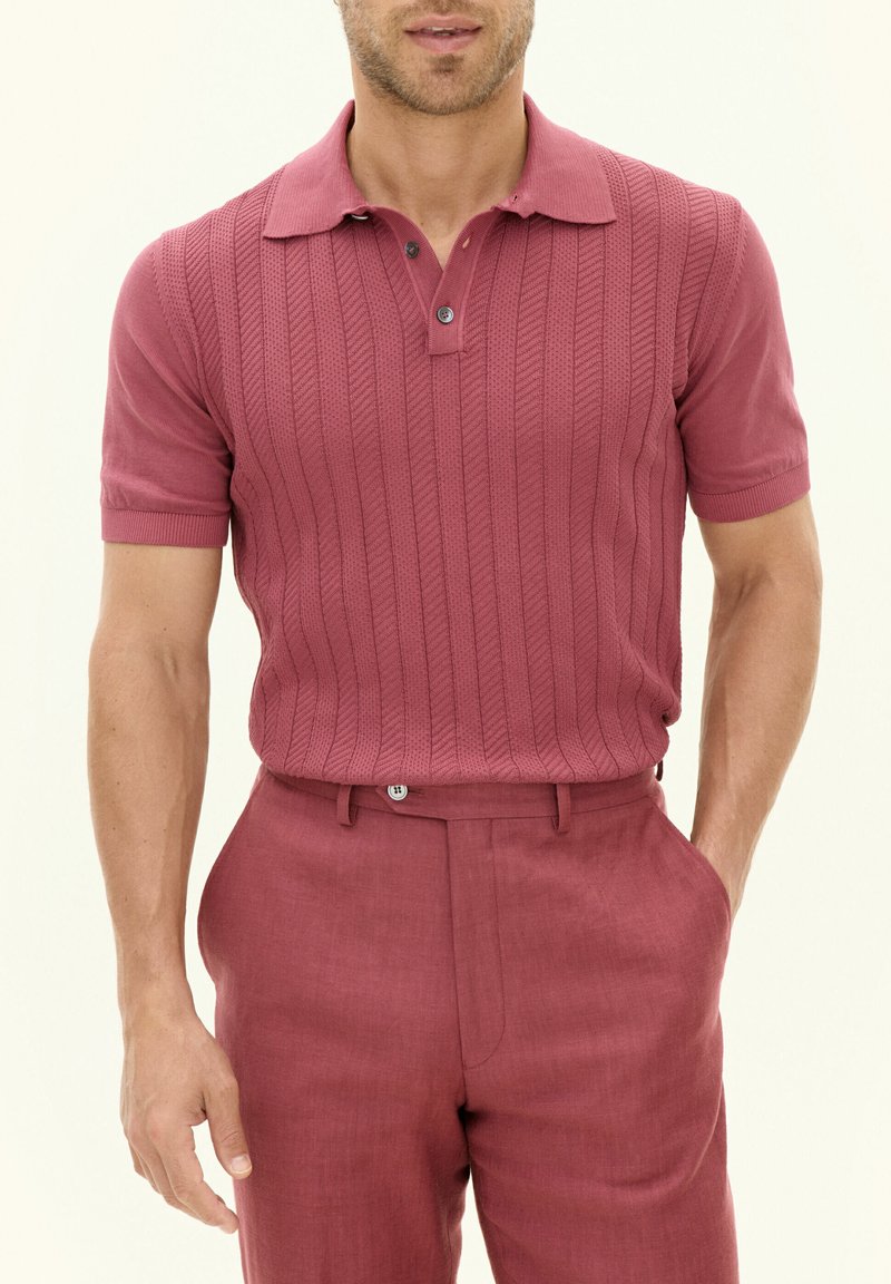 Polo shirt lavorato a maglia di un rosa scuro con un motivo a righe verticali testurizzate, abbinato a pantaloni su misura dello stesso colore, con pince frontale e passanti per cintura.