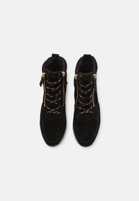 Schwarze Wildleder-Ankle-Boots mit Schnürsenkeln, zwei goldenen Reißverschlussakzenten, weicher Fütterung und strukturiertem Profil. Mit einem Ziehverschluss an der Rückseite für ein einfaches An- und Ausziehen.