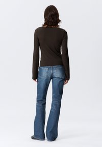 Μπλούζα μακρυμάνικη σε σκούρο καφέ χρώμα συνδυασμένη με ανοιχτό μπλε τζην παντελόνι με φαρδιά καμπάνα, με κλασική εφαρμογή και διακριτική υφή τζην.