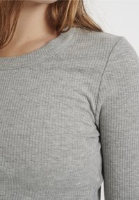 Graues, geripptes Langarmshirt mit rundem Ausschnitt, weicher Textur und figurbetonter Silhouette, das dezente Variationen im Stoff zeigt.