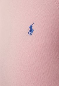 Tejido de punto rosa con una superficie texturizada que presenta un pequeño logo bordado en azul de un caballo y un jinete.