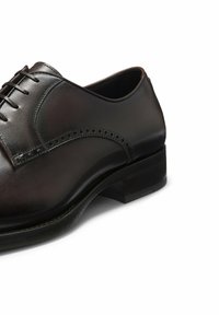 Scarpa da uomo in pelle nera con punta arrotondata, design con lacci, accenti decorativi con perforazioni e un robusto tacco a blocco.