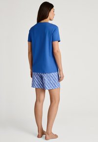 Blauwe katoenen t-shirt gecombineerd met patroon blauwe en witte shorts met een geometrisch ontwerp. Zachte textuur, korte mouwen en een relaxed fit.