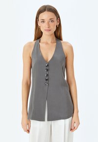 Grijze haltertop met een diepe V-hals en zes zwarte knopen aan de voorkant. Lichtgewicht stof met een gladde textuur, voorzien van zijslits.