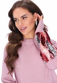 Różowy sweter z prążkowanym dekoltem i długimi rękawami, zdobiony cekinami w czerwonym, srebrnym i różowym kolorze w falisty wzór na rękawach.