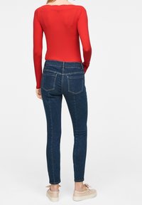 Czerwony body z długim rękawem w połączeniu z obcisłymi, ciemnoniebieskimi jeansami z wysokim stanem, posiadającymi dwie tylne kieszenie i bezszwową talię.