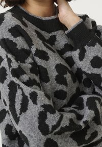 Pull gris en maille avec un motif léopard noir, col rond et tissu texturé avec des manches légèrement surdimensionnées.