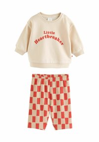 Hellbeiges Sweatshirt mit rotem Text "Little Heartbreaker", kombiniert mit gerippten Shorts in Rot-Beige-Karomuster.