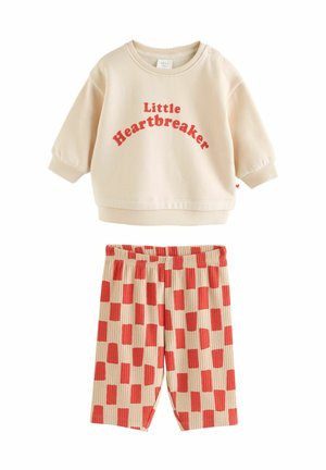Light beige sweatshirt with "Little Heartbreaker" in red text, paired with ribbed shorts featuring a red and beige checker pattern.