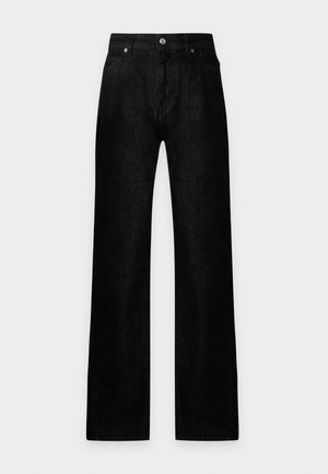 Femme portant un t-shirt graphique rouge, un jean noir droit, des bottines noires et tenant un sac à épaule noir.