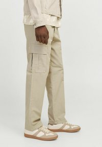 Beige cargos lavet af bomuld, med sidelommer og en afslappet pasform, parret med tan og hvide sneakers med strukturerede detaljer.