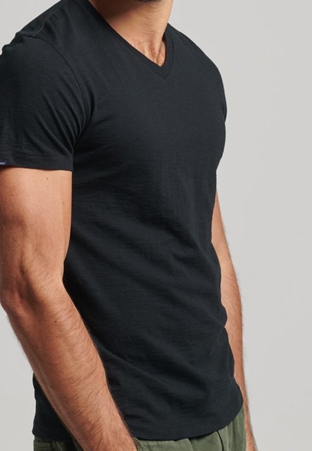 T-shirt nera con scollo a V realizzata in tessuto leggero. Presenta una vestibilità slim e maniche corte. Texture liscia, branding minimale vicino all'orlo.