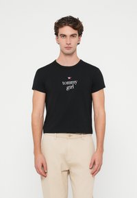 Černé bavlněné tričko s krátkým rukávem a kulatým výstřihem. V centru se nachází nápis "tommy girl" a malé hvězdné logo.