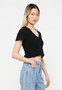 Haut noir court à boutons avec un motif texturé, manches courtes et décolleté en V, associé à un jeans taille haute bleu clair.