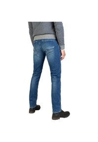 Jeans de denim azul con un diseño ajustado, que presentan una cintura de mediana altura, bolsillos traseros y un acabado deslavado. El conjunto se completa con zapatos negros.