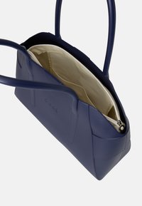 Borsa sintetica blu navy con texture liscia, doppio manico e interni beige chiaro, dotata di una tasca con zip e design elegante.