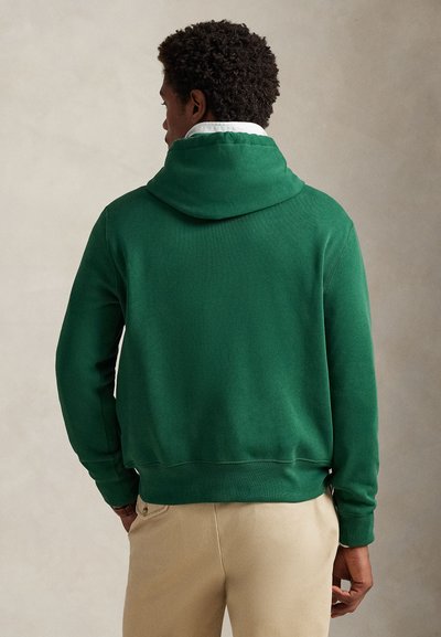 Zelena majica s kapuljačom od mekog tkanja, s kangur džepom i rebrastim manžetnama. Dizajn je opuštenog kroja s polovinom dužine siluete.