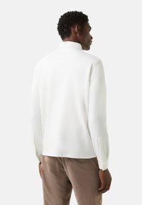 Weißes Langarmhemd mit spitzem Kragen, glatter Textur und Knopfmanschetten, kombiniert mit hellbraunen Hosen. Verfügt über ein minimalistisches Design.