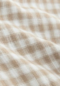 Țesătură țesută cu un model în carouri bej și alb, având o textură netedă și un design de grilaj vizibil.