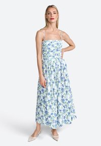 Bloemige maxi-jurk met lichtblauwe en groene patronen, strak aangetrokken lijfje, spaghettischouderbandjes en een vloeiende rok. Draag met beige schoenen.