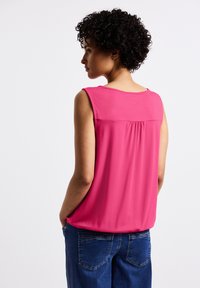 Top senza maniche di colore rosa con una texture morbida, presenta un pannello posteriore arricciato e una scollatura rotonda. Abbinato a jeans in denim blu.