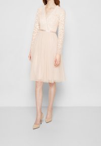 Abito a maniche corte a forma ad A in rosa chiaro con corpino di pizzo, motivi floreali in paillettes e gonna in tulle a strati. Presenta una vita da abbinare.