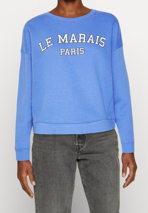 Blå sweatshirt med ribbade ärmslut och nederkant, med vit broderad text "LE MARAIS PARIS" i en böjd format. Texturerad tyg.