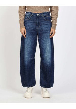 Person wearing high-waist, wide-leg blue jeans with faded front and white sneakers, paired with a beige cropped sweater.