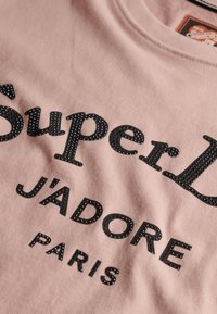 Różowy bawełniany t-shirt z czarnym, fakturowanym nadrukiem "Super L J'adore Paris" ozdobionym małymi czarnymi kryształkami.